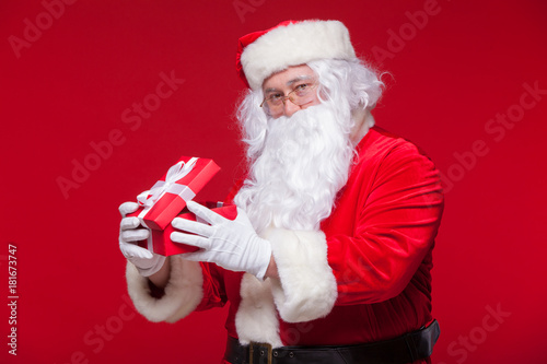 Christmas. Photo Santa Claus giving xmas present and looking at camera, on a red background photo