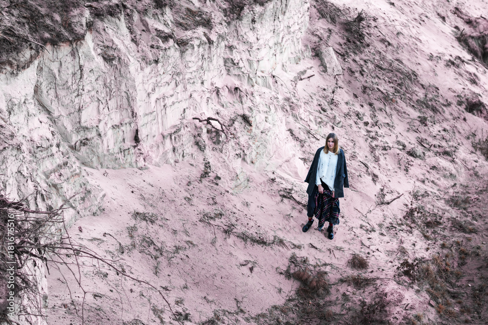 Woman in a sweater and a coat at the bottom of a sand pit, in the distance Woman in a sweater and a coat at the bottom of a sand pit, in the distance