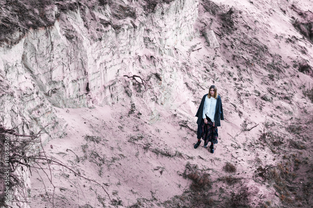 Woman in a sweater and a coat at the bottom of a sand pit, in the distance