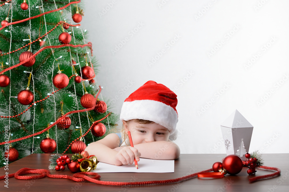A letter to Santa Claus concept. Cute little girl with a pen at the table by the Christmas tree