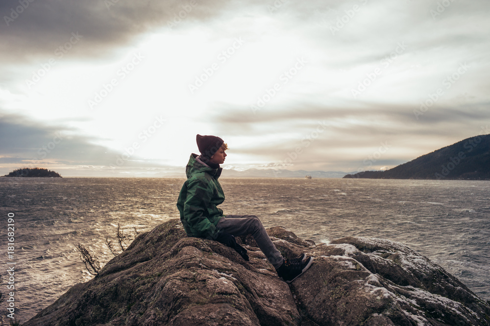 Boy sitting on rock overlooking the ocean