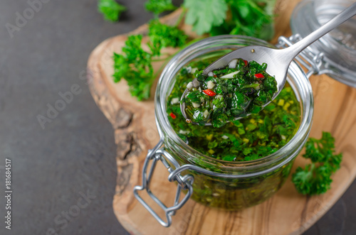Traditional argentinian chimichurri sauce made of parsley, cilantro, garlic and chili pepper in a glass jar, focus on a spoon with sauce. Selective focus, horizontal image photo