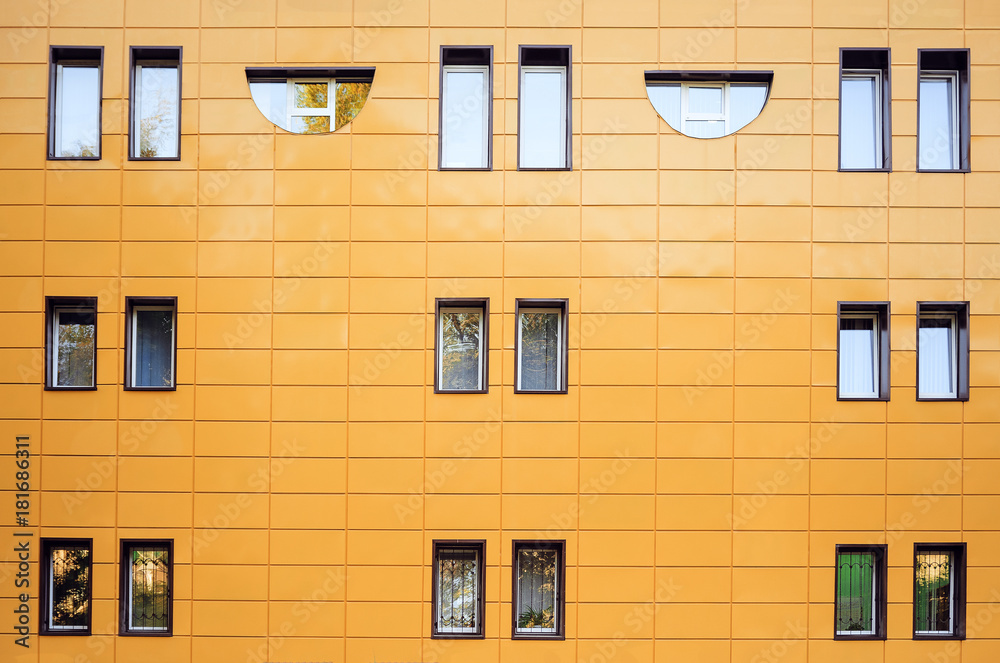 Fototapeta premium Fragment of a orange wall with windows. Front view. A strict laconic style.