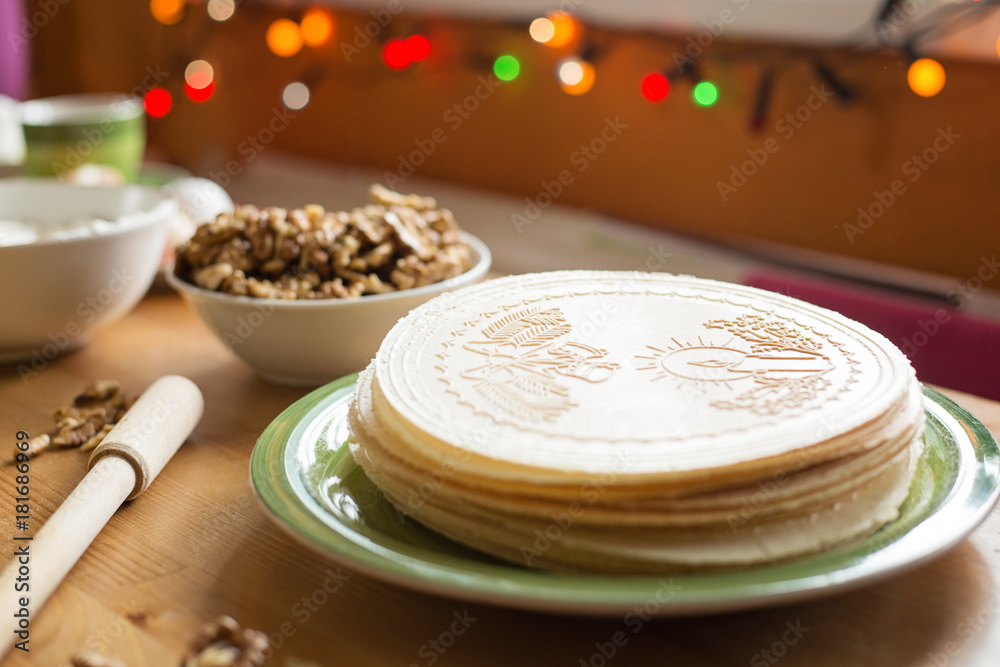 Christmas wafers placed on a wooden kitchen table, on a green plate next to a window. Wafers are round, cream color, surrounded by ingredients Christmas wafers placed on a wooden kitchen table, on a green plate next to a window. Wafers are round, cream color, surrounded by ingredients