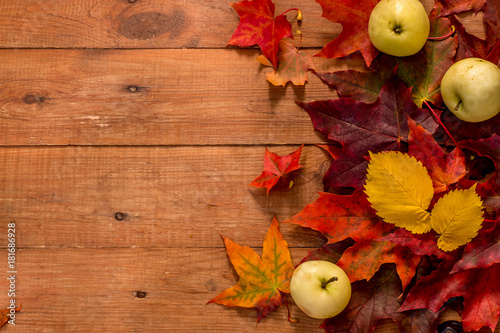 brown wooden background with bright red and yellow autumn leaves and apples
