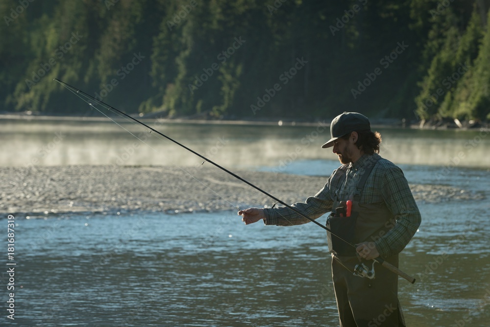 Man adjusting reel while fishing in river Man adjusting reel while fishing in river
