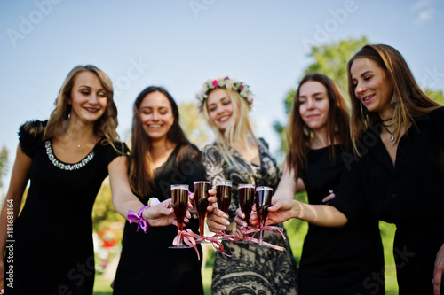 Five girls wear on black with balloons drinking red champagne at hen party.