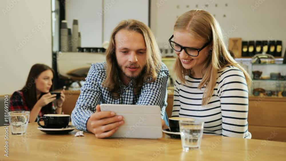 Happy young couple holding a digital tablet computer and looking at it in the coffee cafe, feeling happy and satisfied. Close up shot. Happy young couple holding a digital tablet computer and looking at it in the coffee cafe, feeling happy and satisfied. Close up shot.