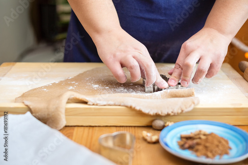 Female hands cutting a cookie with a cookie cutter. Dough is placed on the wooden board, on the wooden kitchen table
