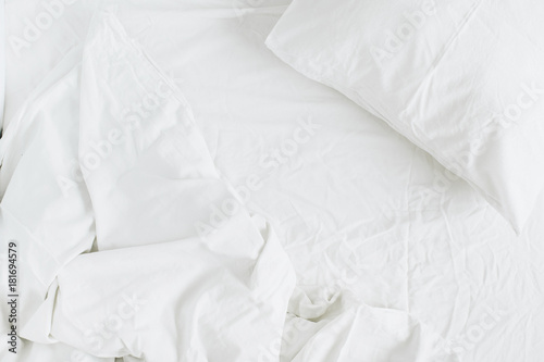 Flat lay of white bed with pillows, blanket and sheet. Top view minimal linen concept.