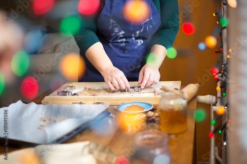 Young woman baking ginger bread at home, christmas lights at the foreground.