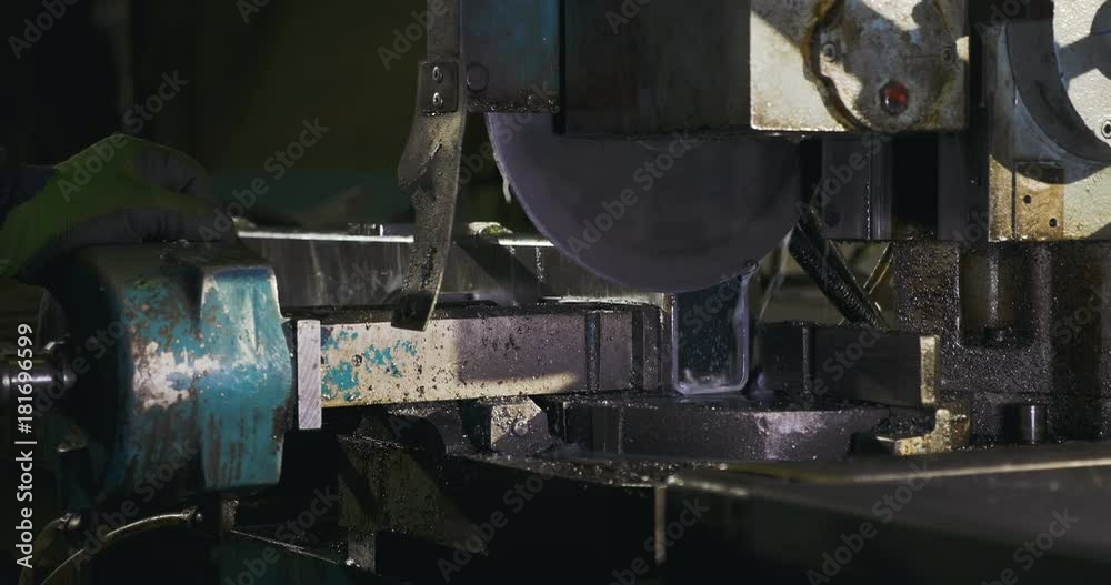 A metal cutting saw at an automotive shop slowly drops down as it begins to cut a piece of metal. The camera moves to the right. A metal cutting saw at an automotive shop slowly drops down as it begins to cut a piece of metal. The camera moves to the right.