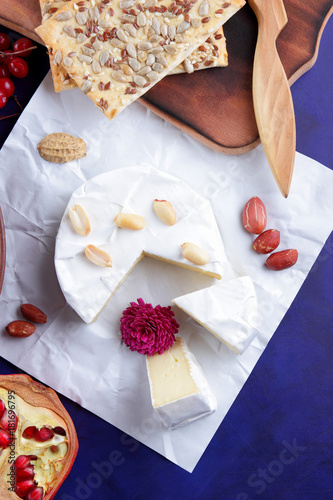Cheese, soft camembert cheese, red berries, pomegranate, peanut grains, flower, biscuits, white cheese on a blue background, wooden board, pop art, retro style