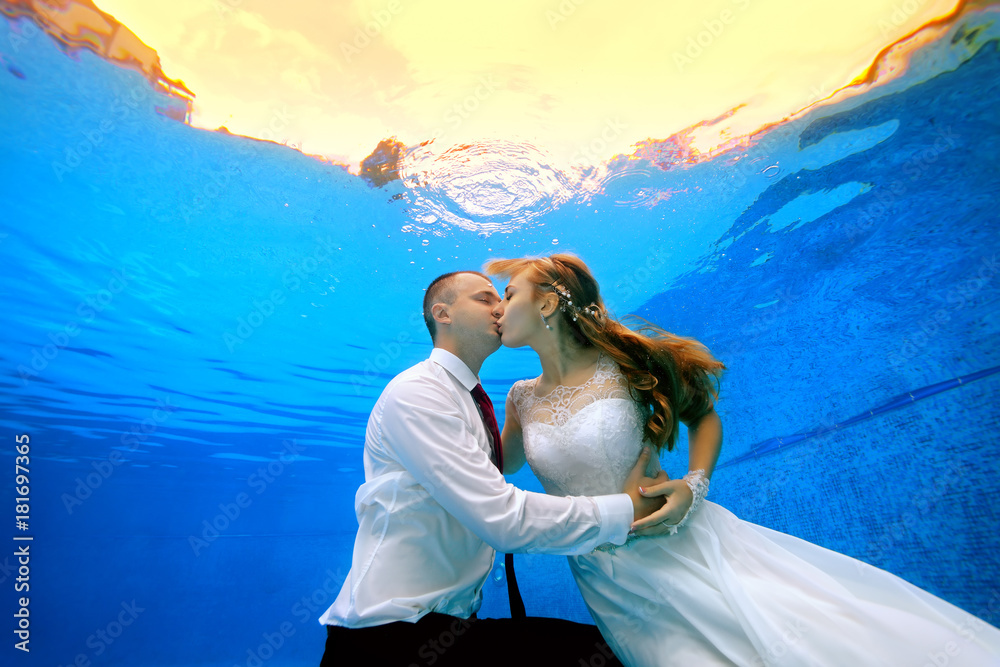 Happy man and woman in wedding dresses kissing underwater in the swimming  pool on the background of a tropical sunset. Horizontal view. Shooting  under water Stock Photo | Adobe Stock