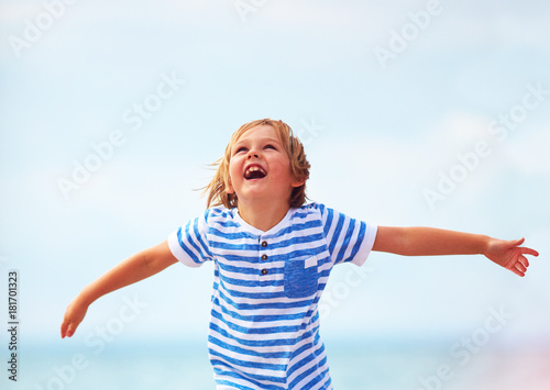 cute emotional kid, boy shining with happiness, running through the sandy beach