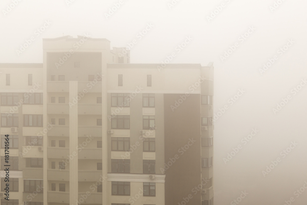 Top part of highrise modern apartment building facade during heavy fog weather Top part of highrise modern apartment building facade during heavy fog weather