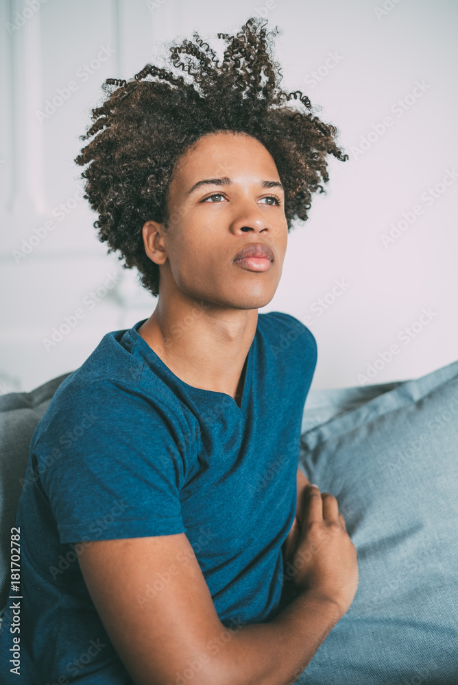 Fototapeta premium Portrait of a young thoughtful mixed race man sitting in the sofa