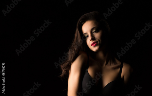 Studio portrait of pretty woman with bright makeup posing with naked shoulders in the dark
