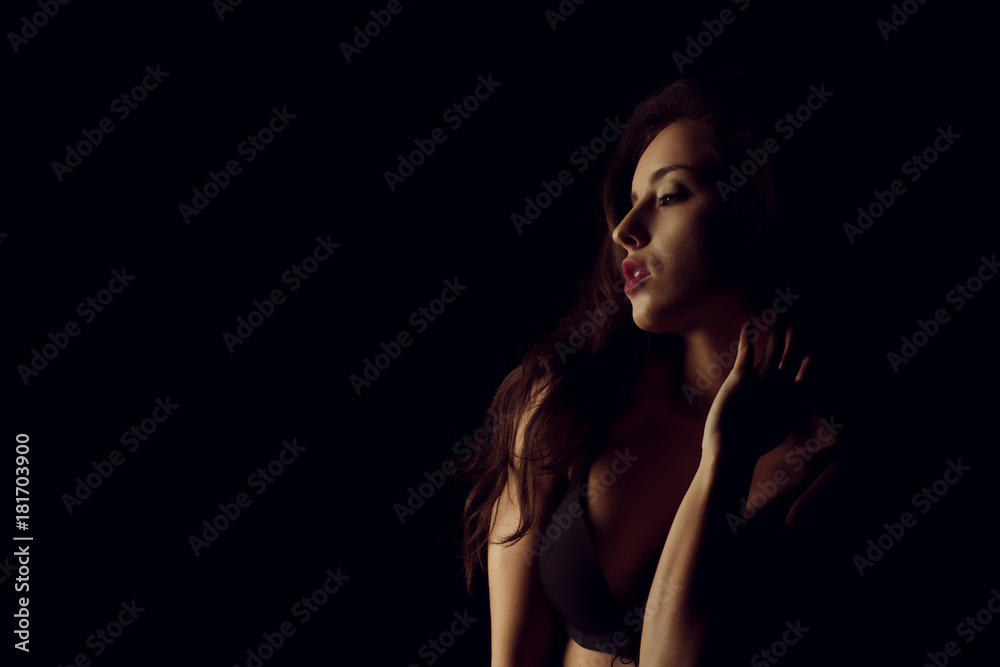 Studio portrait of beautiful young woman with bright makeup posing with naked shoulders in the dark