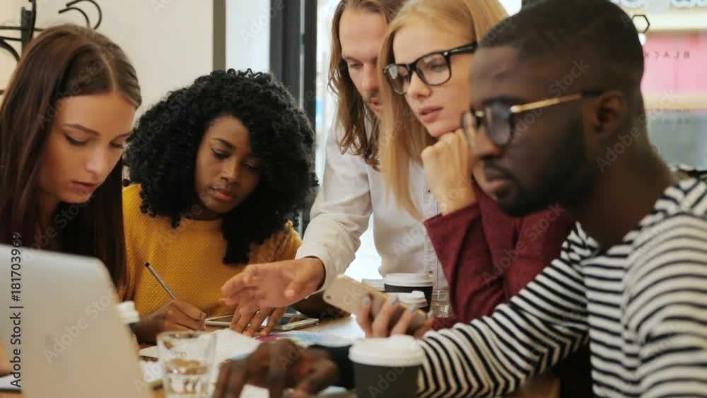 Close up shot of young creative students in casual clothes working together, typing information for the start-up project on the laptop in a cafe.