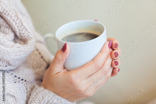 Beautiful woman holding a cup of coffee in her hands. in a knitted beige sweater