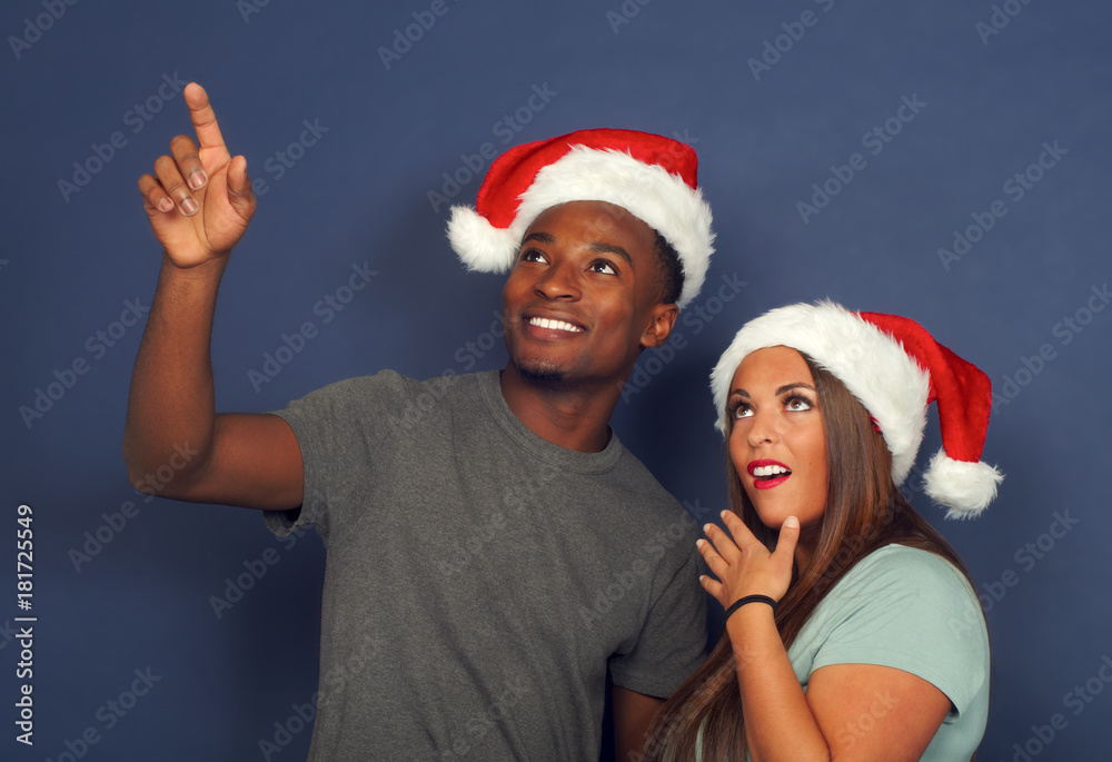 surprised women man pointing up christmas red hat santa claus december holiday party young couple surprised women man pointing up christmas red hat santa claus december holiday party young couple