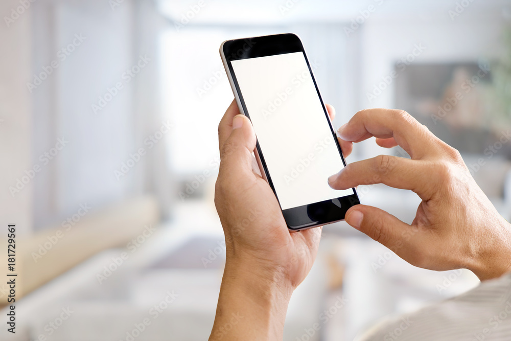 Mockup image of hands holding black mobile phone with blank white screen in living room. Mockup image of hands holding black mobile phone with blank white screen in living room.