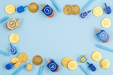 Blue background with multicolor dreidels, menora candles and chocolate coins. Hanukkah and judaic holiday concept.