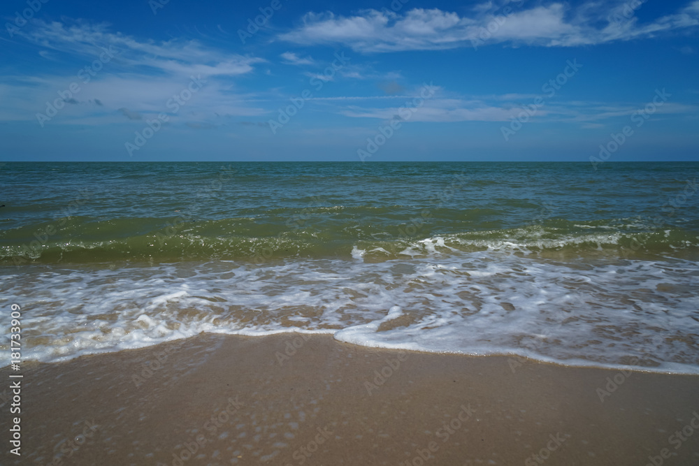 Soft foam slow sea wave on white sand beach with blue sky and white cloud background