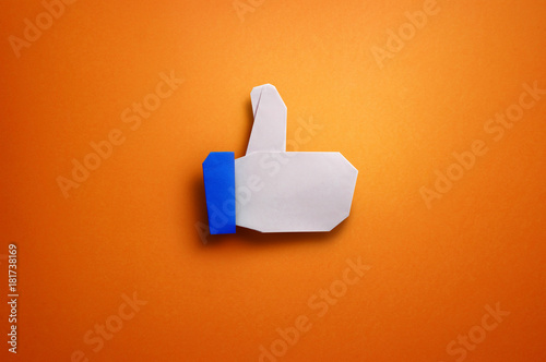 Origami thumbs up paper craft on orange background photo