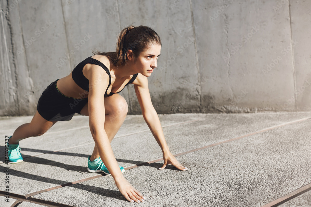 Fototapeta premium Portrait of young fit runner ready to take off. Woman taking care about her sporty body.