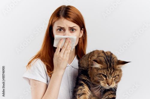 Beautiful young woman on a light background holds a cat, an allergy to pets