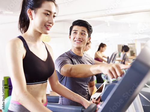 young asian adults exercising on treadmill helped by male trainer