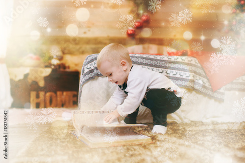 Little child boy in black and white pajamas on the floor with book fairy tales near Christmas tree in decorated New Year wooden room at home. Family and holiday 2018 concept. Magical highlight effect