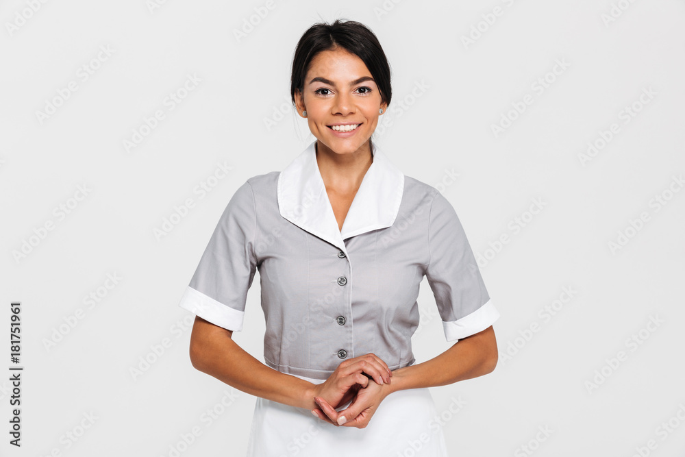 Portrait of pretty smiling maid in uniform keeping hands together and looking at camera Portrait of pretty smiling maid in uniform keeping hands together and looking at camera