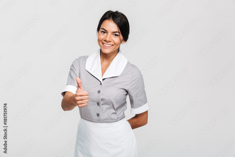 Cheerful brunette housekeeper in uniform showing thumb up gesture and looking at camera Cheerful brunette housekeeper in uniform showing thumb up gesture and looking at camera