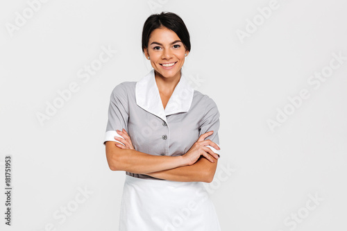 Close-up portrait of young smiling housekeeper in uniform standing with crossed hands and looking at camera photo