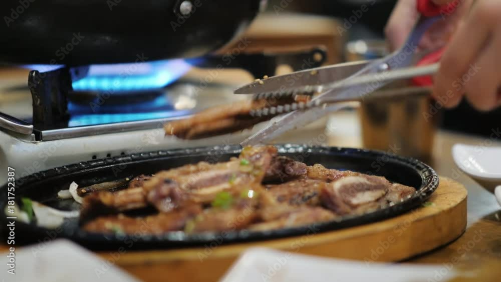 A woman uses tongs and scissors to cut food. Starts a meal in a Korean restaurant. Korean cuisine concept A woman uses tongs and scissors to cut food. Starts a meal in a Korean restaurant. Korean cuisine concept