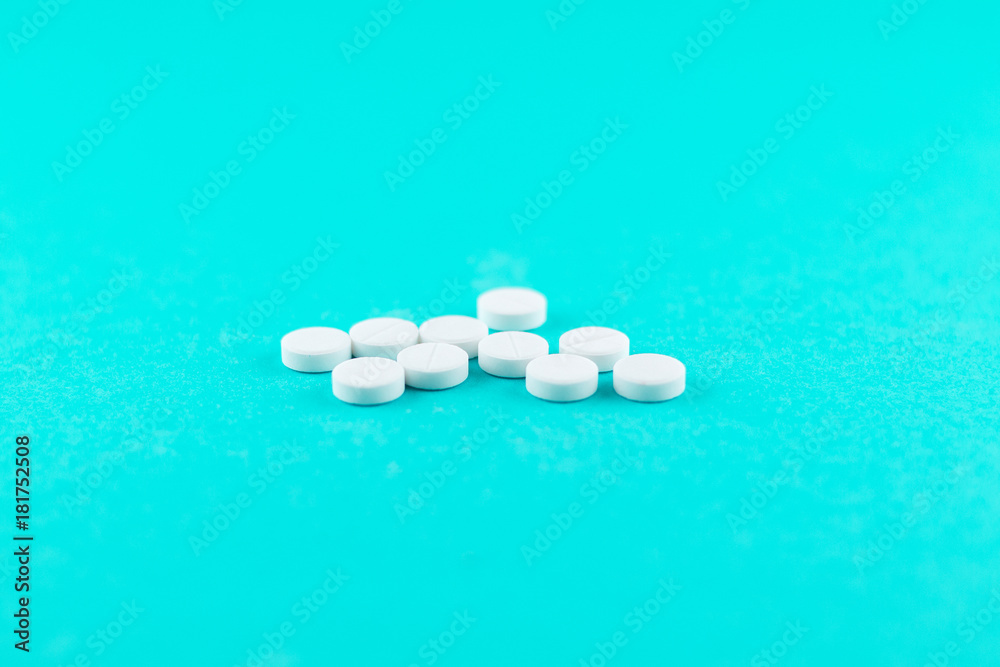 White pills with copy space on turquoise background. Focus on foreground, soft bokeh. Pharmacy drugstore concept