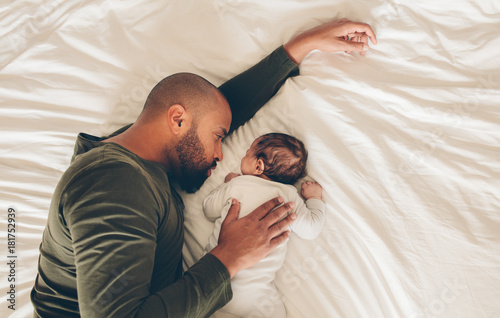 Newborn baby boy sleeping with his father on bed photo