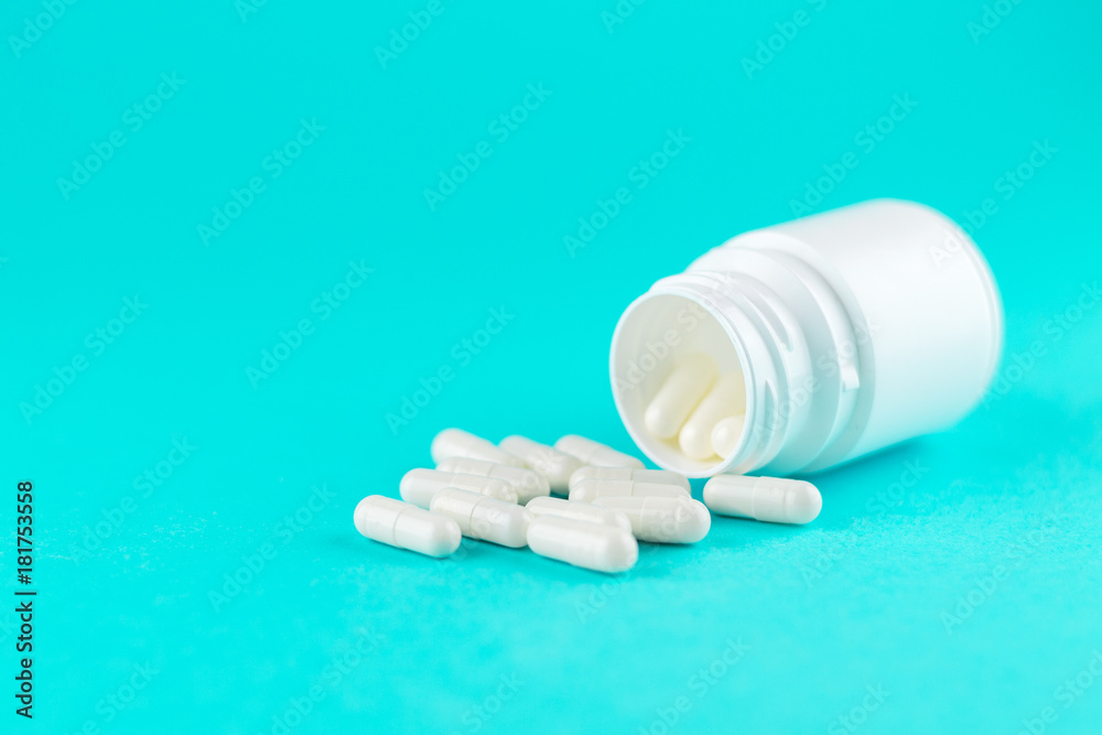 Close up white pill bottle with spilled out capsules on turquoise background with copy space. Focus on foreground, soft bokeh. Pharmacy drugstore concept Close up white pill bottle with spilled out capsules on turquoise background with copy space. Focus on foreground, soft bokeh. Pharmacy drugstore concept