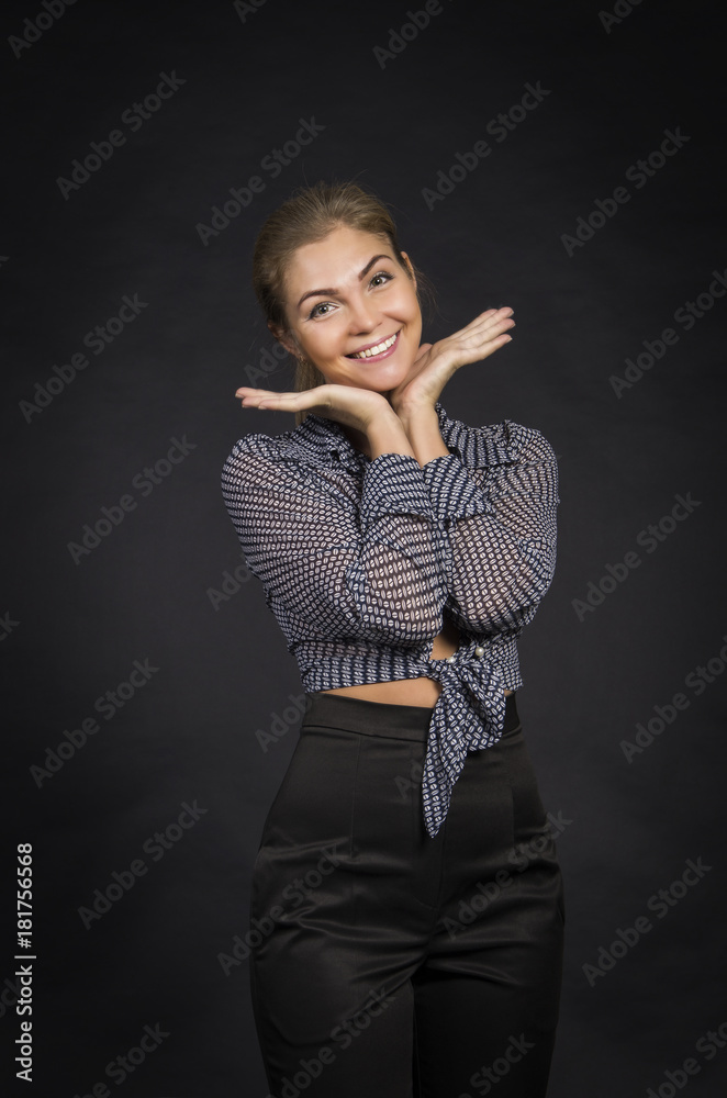 Fototapeta premium Emotional girl in a shirt and black pants posing on dark background.