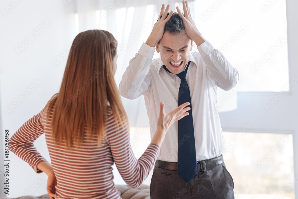 Emotional quarrel. Angry irritated emotional man standing in a light room and closing his head with his hands while rejecting to hear stupid arguments of his wife during their quarrel Emotional quarrel. Angry irritated emotional man standing in a light room and closing his head with his hands while rejecting to hear stupid arguments of his wife during their quarrel