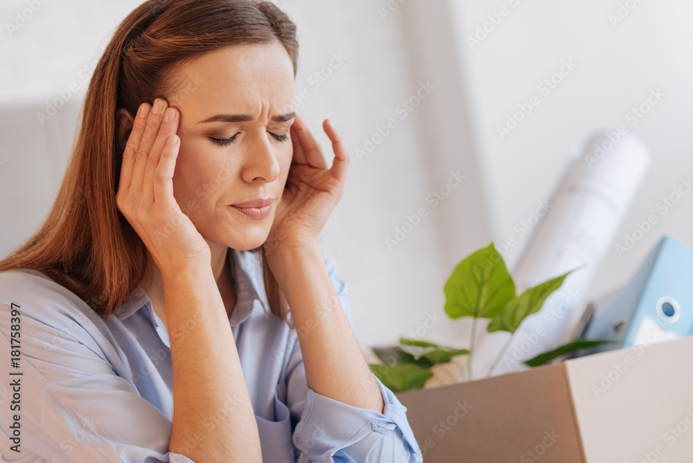 Pain. Emotional sensitive young woman sitting with her eyes closed while having a terrible headache after finding out the information about her dismission Pain. Emotional sensitive young woman sitting with her eyes closed while having a terrible headache after finding out the information about her dismission