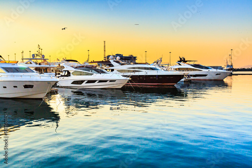 Luxury yachts docked in sea port at sunset. Marine parking of modern motor boats and blue water. Travel and fashionable vacation.