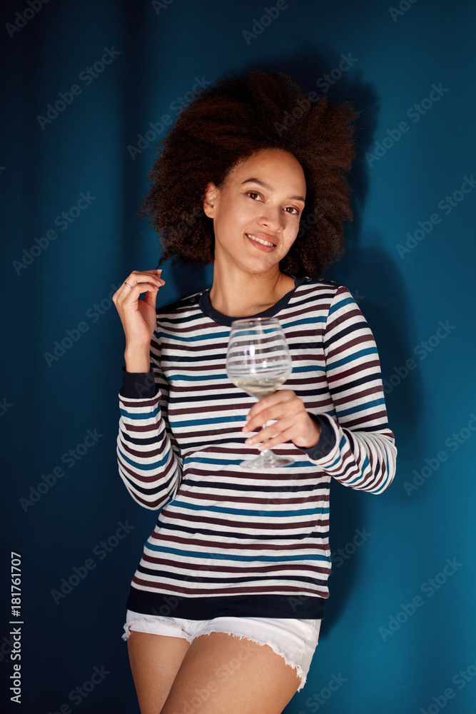 Portrait of mixed race woman holding wineglass while standing in front of blue wall Portrait of mixed race woman holding wineglass while standing in front of blue wall