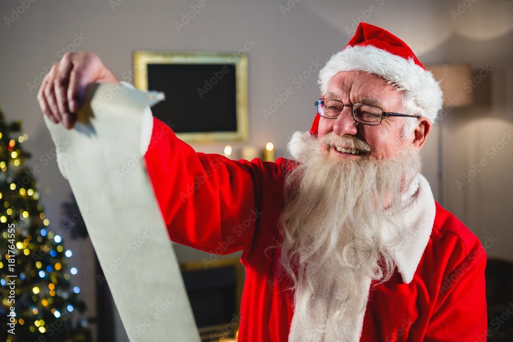 Naklejka premium Santa Claus reading scroll in living room