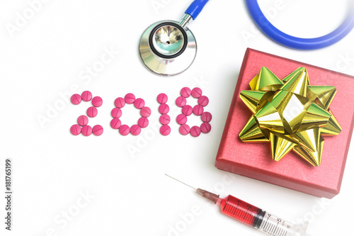 Medical pills with red gold gift box, stethoscpoe, and injection on white background.  Word 2018 made from pink pharmaceutical tablets . photo