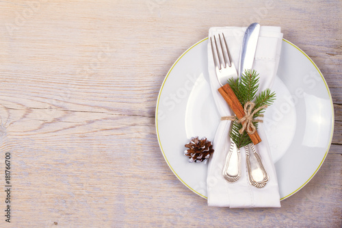 Christmas set with plate, cutlery, pine branches, cinnamon and red berries on wooden place. Winter holidays and festive background. Christmas eve dinner, New Year food lunch. View from above, top