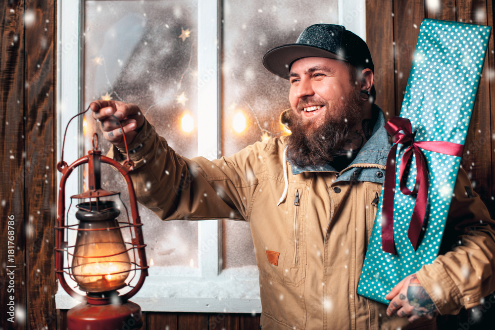Christmas night, snow falling, funny man with a beard and with gifts in hand and flashlight at the window. Winter background